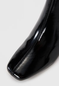 Schwarzer Lackleder-Stiefelette mit einer eleganten, quadratischen Spitze, glatter Oberfläche und sichtbaren Nähten entlang der Seitennaht.