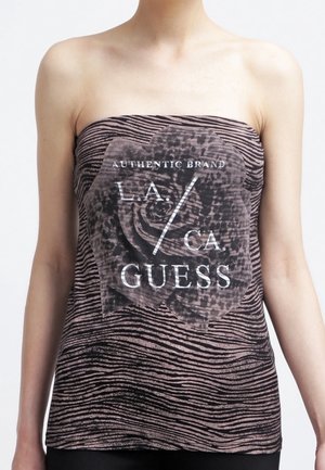 Persoon draagt een strapless bruin-zwart gestreept topje met een grote bloem en de tekst "Authentic Brand L.A./CA GUESS" aan de voorkant.