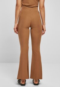 Pantalons évasés marron côtelés avec une taille haute et une coupe ajustée, présentant des rayures verticales et une texture lisse.