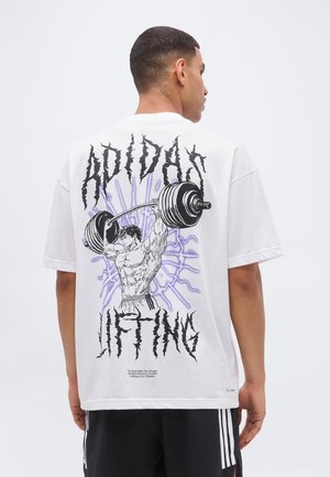 Mężczyzna ubrany w białą koszulę z grafiką muskularnej postaci podnoszącej ciężki sztangę oraz tekstem „Adidas Lifting” na plecach.