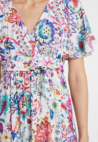 Blomsterkjole i let stof med livlige flerfarvede mønstre, V-halsudskæring og justerbar bælte i taljen.