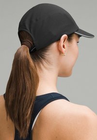 Gorra negra con un diseño elegante, visera curva y tela texturizada. Diseñada para llevar con coleta, combinada con una camiseta atlética azul marino.