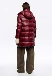 Bordowa puchowa kurtka z kapturem, charakteryzująca się błyszczącym pikowanym wzorem, szerokimi rękawami oraz ozdobami z futerka na mankietach.