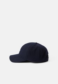 Cappellino da baseball in lana di un blu navy scuro con una corona arrotondata e una visiera rigida. Presenta cuciture tono su tono e una regolazione sul retro.