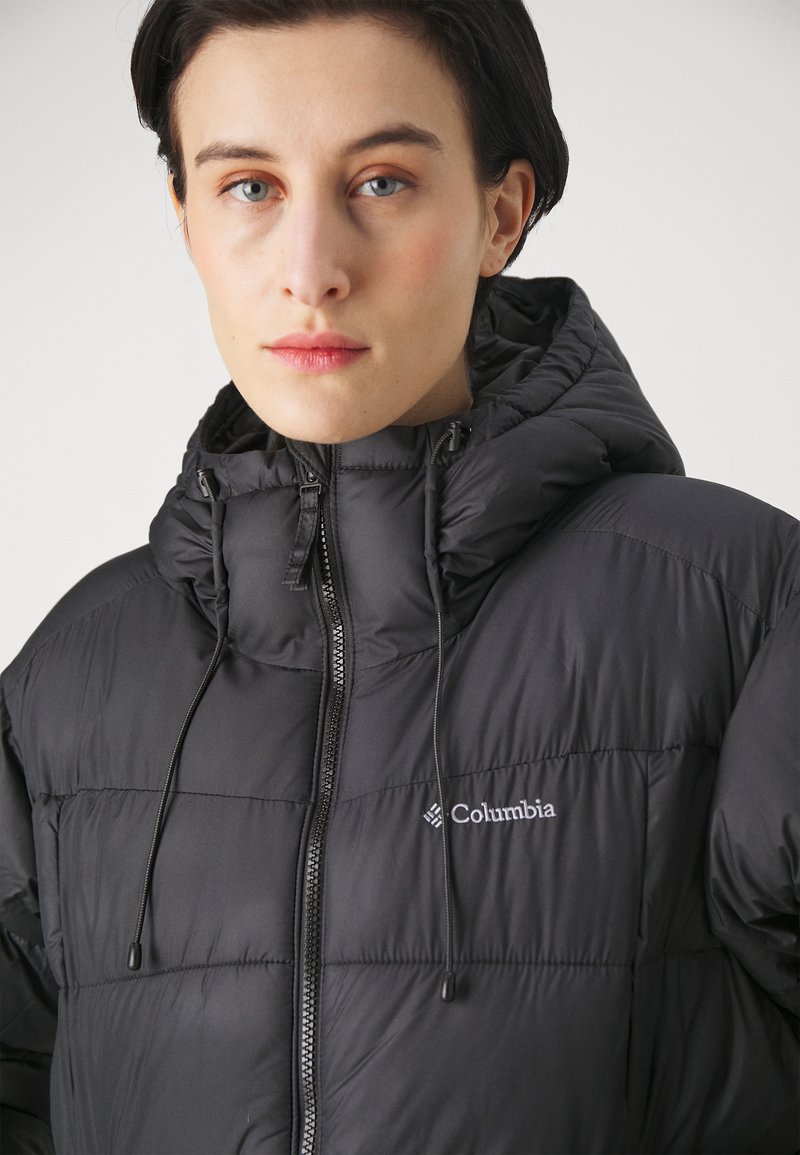 Chaqueta acolchada negra con capucha, con un diseño acolchado, cordones ajustables y un logo plateado de Columbia en el pecho.