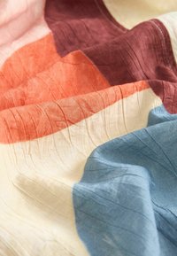 Tissu doux et froissé avec des blocs de couleurs bleu, crème, orange et bordeaux dans une disposition fluide et pliée.