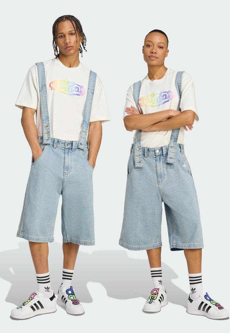 Denim kombinézy s širokými nohavicami a nastaviteľnými popruhmi, kombinované s bielymi tričkami s farebnými grafickými dizajnmi. Čierno-biele tenisky.