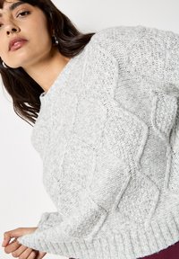Jasnoszary sweter dziany z fakturowanym wzorem w romby, okrągłym dekoltem i ściągaczami, o miękkim i przytulnym wykończeniu.