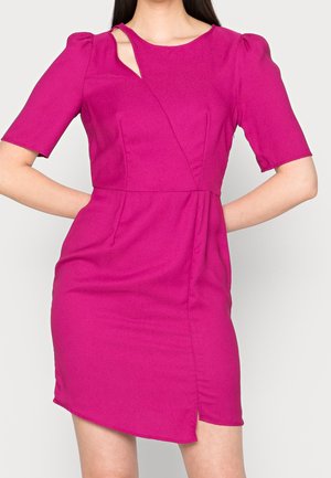 Donna che indossa un vestito rosa acceso a maniche corte con uno spacco diagonale vicino allo scollo e un orlo asimmetrico.