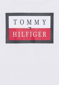 White T-shirt featuring a rectangular logo in red, white, and navy, with the texts "TOMMY" above and "HILFIGER" below, separated by a line.