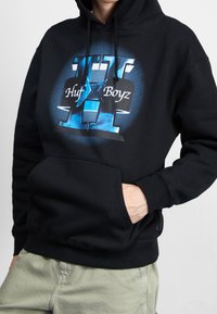 Sudadera con capucha negra que presenta un estampado gráfico con acentos en azul y blanco. Incluye un bolsillo frontal y puños de canalé.