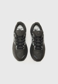 Baskets de sport noires avec une tige en mesh et des accents texturés, dotées d'une semelle rembourrée, d'une fermeture à lacets et d'un détail de logo sur le côté.