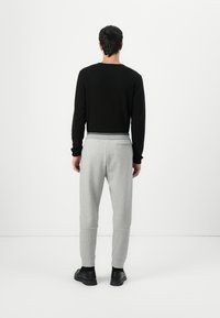 Svart langermet skjorte kombinert med grå joggebukser med innsnevrede ben, elastisk midje og svarte sko. Minimalistisk design.