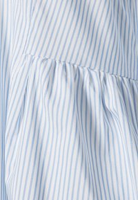 Tissu rayé bleu clair et blanc avec une section froncée, présentant une texture lisse avec des lignes verticales et des détails subtils de plis.