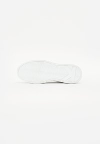 Semelle de sneaker blanche avec un motif de relief ondulé, en matériau caoutchouc et un design plat. Présente un logo et une légère élévation de talon.