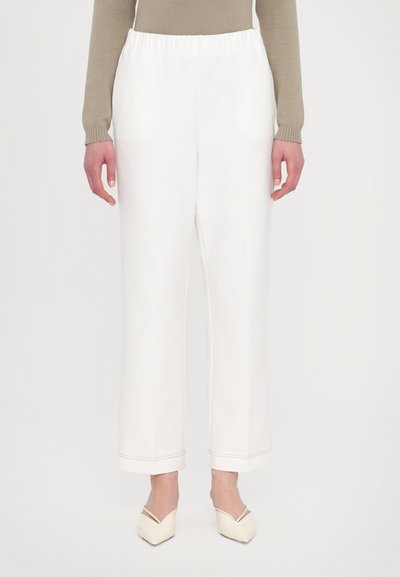 Pantalons blancs à jambes larges avec une taille élastique, en tissu uni et avec une couture contrastée à l'ourlet. Accompagnés de chaussures de couleur claire.