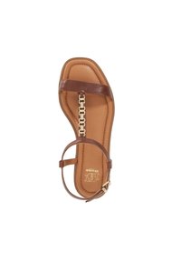 Brown flat sandal featuring a wide strap, a chain-link accent, and an adjustable ankle strap. Soft beige insole with embossed logo detail.