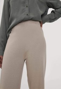 Beige Strickhose mit hohem Bund, kombiniert mit einem hemdenartigen Oberteil in Schiefergrau. Der Stoff wirkt weich und strukturiert.
