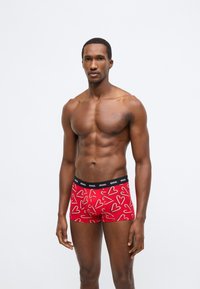 Piros férfi boxeralsó fehér szív- és cukorrúd mintával. Puha anyagból készült, elasztikus fekete derékpánttal, amelyen a márkajelzés látható.