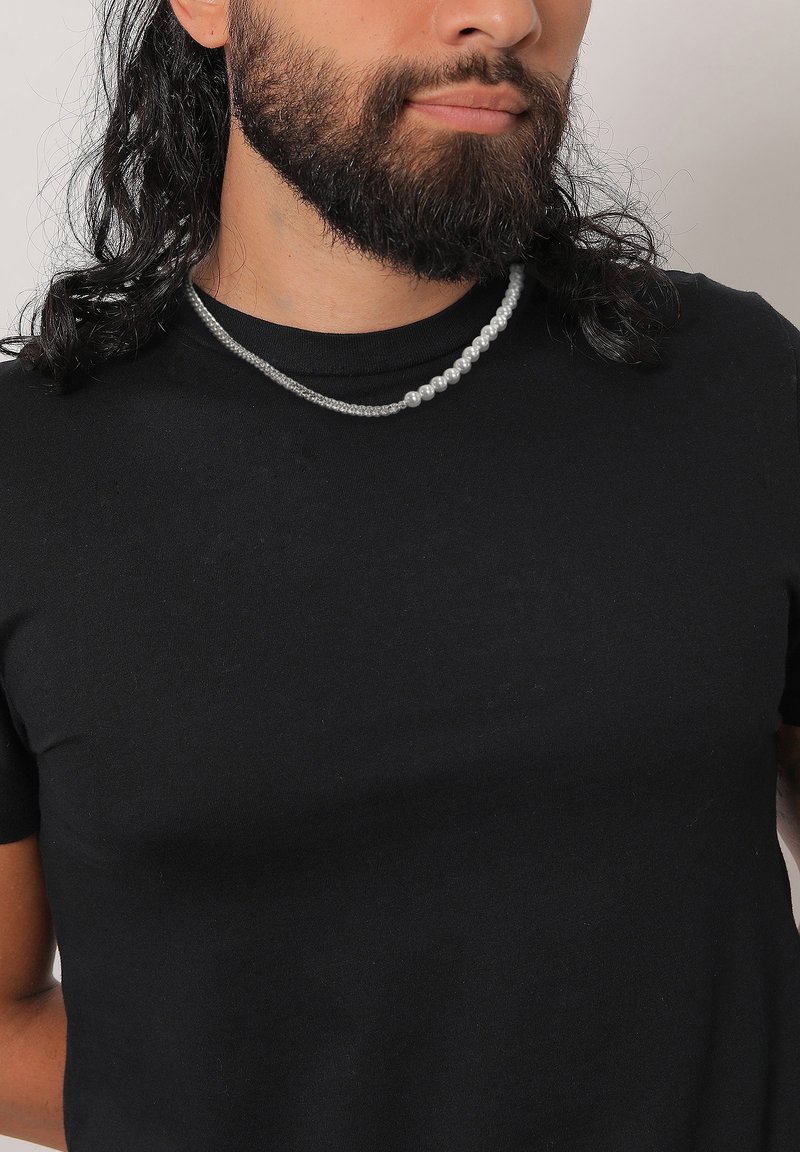 Collana di perle argentate con un design testurizzato indossata sopra una t-shirt nera attillata, caratterizzata da due fili con dimensioni delle perle variabili.