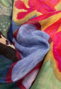 Zachte, lichte stof opgevouwen met kleurrijke bloemen- en abstracte patronen in tinten blauw, rood, geel, groen en roze.