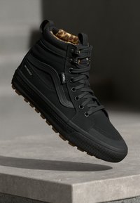Hochschnittige schwarze Vans-Sneaker aus wasserdichtem Material, mit einer strukturierten Gummisohle, kontrastierendem Seitenstreifen und einem Futter im Leopardenmuster.