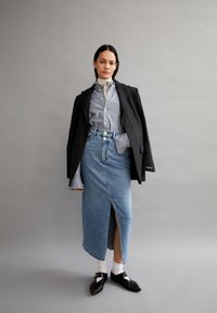 Denimrok met een voorkleur, gedragen met een blauw-wit gestreept shirt, een zwarte blazer en zwarte schoenen met witte sokken. Soepele texturen.