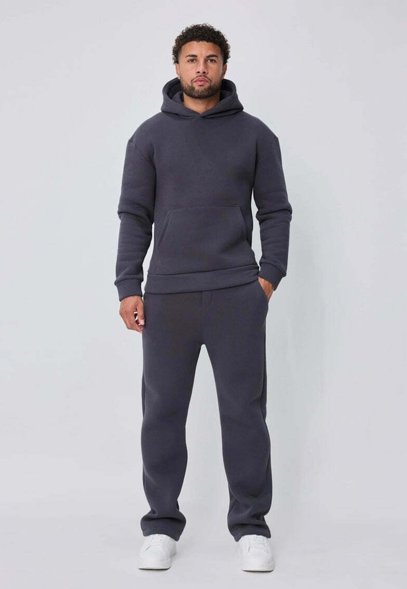 Ensemble sweat à capuche et pantalon de survêtement gris foncé en tissu doux. Comprend une poche kangourou et des poignets côtelés. Complété par des baskets blanches.