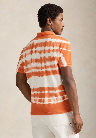 Πόλο μπλουζάκι με κοντά μανίκια σε πορτοκαλί και λευκό μοτίβο tie-dye, με μονόχρωμο πορτοκαλί γιακά και ελαφρώς χαλαρή εφαρμογή. Υφασμένο από υφή βαμβακερού υφάσματος.