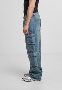 Gai zilas denima cargo bikses ar vairākiem sānu kabatām, brīvas griezuma un nedaudz nolietota tekstūra. Valkātas ar sudraba kedām.