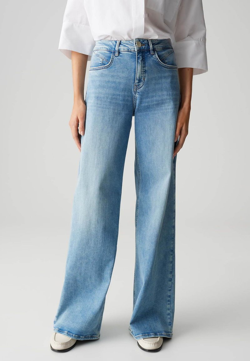 Jean en denim bleu clair à jambe large avec une taille haute, comportant cinq poches, un léger décoloration et une fermeture à bouton à l'avant.