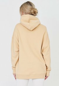 Béžová oversized mikina s kapucí, žebrovanými manžetami a lemem. Měkká textura, volný střih a minimalistické švy.