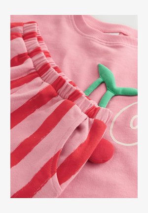 Roze sweatshirt met een groen applicatie-detail, in combinatie met roze shorts met rode strepen. Zachte stof, elastische tailleband en ronde accenten.