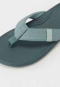 Lys blå flip-flop sandal med teksturert gummisåle, stofftåpost og sømmer på stroppene. Designet for komfort og støtte.