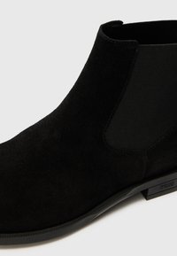 Bottines Chelsea en cuir suédé noir, avec un dessus lisse, des panneaux latéraux élastiques et un talon bas. Surface texturée avec une silhouette élégante et moderne.