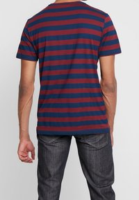 T-shirt rayé rouge et marine en coton, avec un col rond, des manches courtes et une coupe décontractée. Vue de dos, montrant l'ourlet et les coutures.