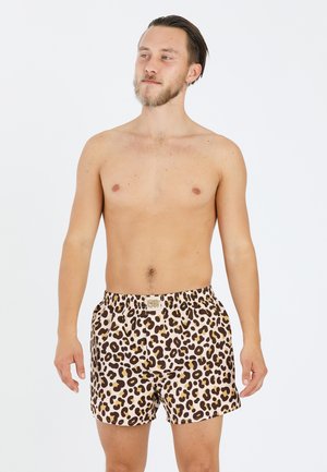 Leopard-print swim shorts made of lightweight fabric, featuring an elastic waistband, beige background, and brown and black spots.