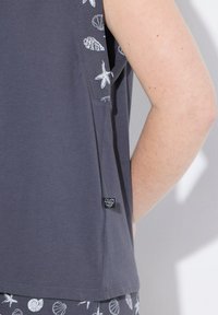 Graues ärmelloses Top mit weißen Muschel- und Seesternmustern entlang des Armausschnitts; enthält ein kleines schwarzes Markenlabel am unteren Ende.