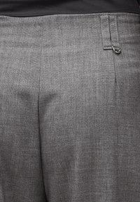 Κοντινό πλάνο γκρι παντελονιών με ζώνη μέσης και θηλιά ζώνης που διαθέτει μικρή μεταλλική λεπτομέρεια σε σχήμα δακτυλίου.