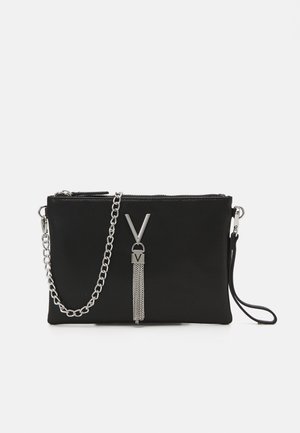 Sort tekstureret clutch-taske med lynlåslukning, sølvkæderem og en dekorativ kvast med et V-formet accent.