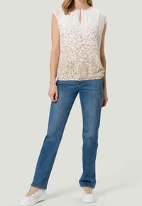 Blusa blanca de flores con mangas cortas y escote de llave, combinada con jeans rectos azules y zapatillas blancas con cordones beige.