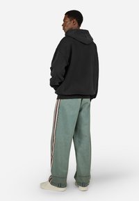 Čierna mikina s kapucňou, voľný strih, skombinovaná s svetlomodrými širokými džínami so bočnými pruhmi. Biely tenisky dopĺňajú outfit.