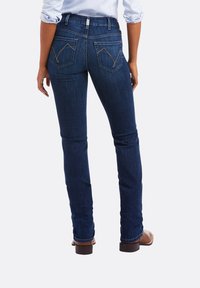 Pantalones vaqueros de mezclilla azul oscuro con un corte ajustado, que cuentan con dos bolsillos traseros con un patrón de costura en zigzag y una cinturilla de altura media.