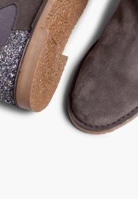 Dwa buty z teksturowaną brązową gumową podeszwą. Jeden but ma gładką szaro-suede górę, drugi charakteryzuje się purpurowym błyszczącym akcentem.