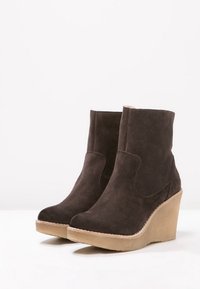 Brown suede wedge ankle boots with a smooth texture, rounded toe, and stitched detailing along the sole and upper.