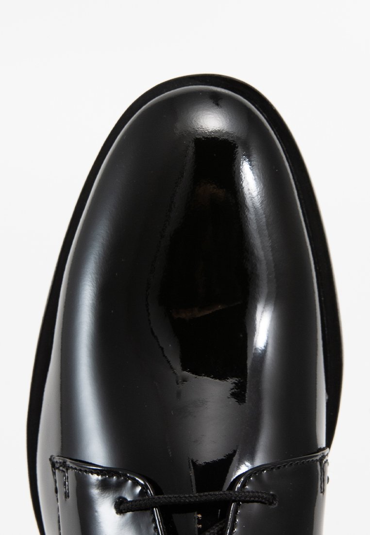 Czarne lakierowane buty o gładkiej, błyszczącej powierzchni, zaokrąglonym nosku i cienkich czarnych sznurkach. Smukły design z minimalną ilością akcentów.