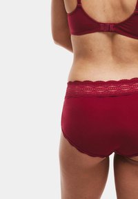 Rode lingerieset met een kanten tailleband, zachte stof en naadloos ontwerp. De slip heeft een gladde afwerking met een delicate golvende rand.