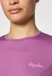 Débardeur de sport violet avec un col rond et des manches courtes. Présente un logo « Rapha. » en rose clair sur la poitrine. Texture lisse.