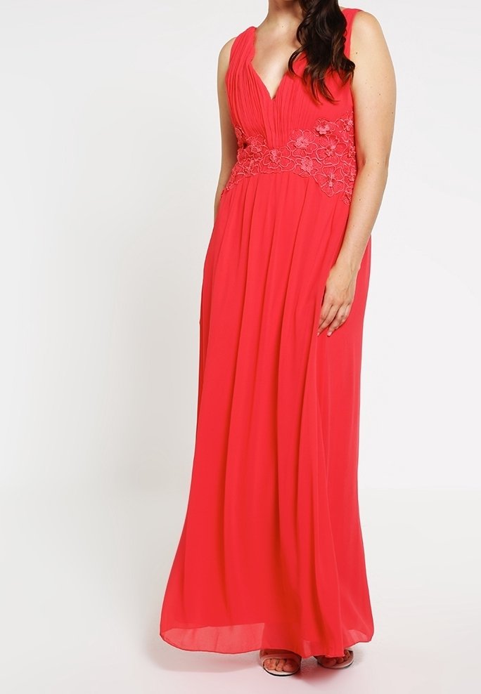 Robe longue corail avec un profond décolleté en V, un corsage plissé et des accents en dentelle fleurie à la taille. Tissu fluide et silhouette décontractée.