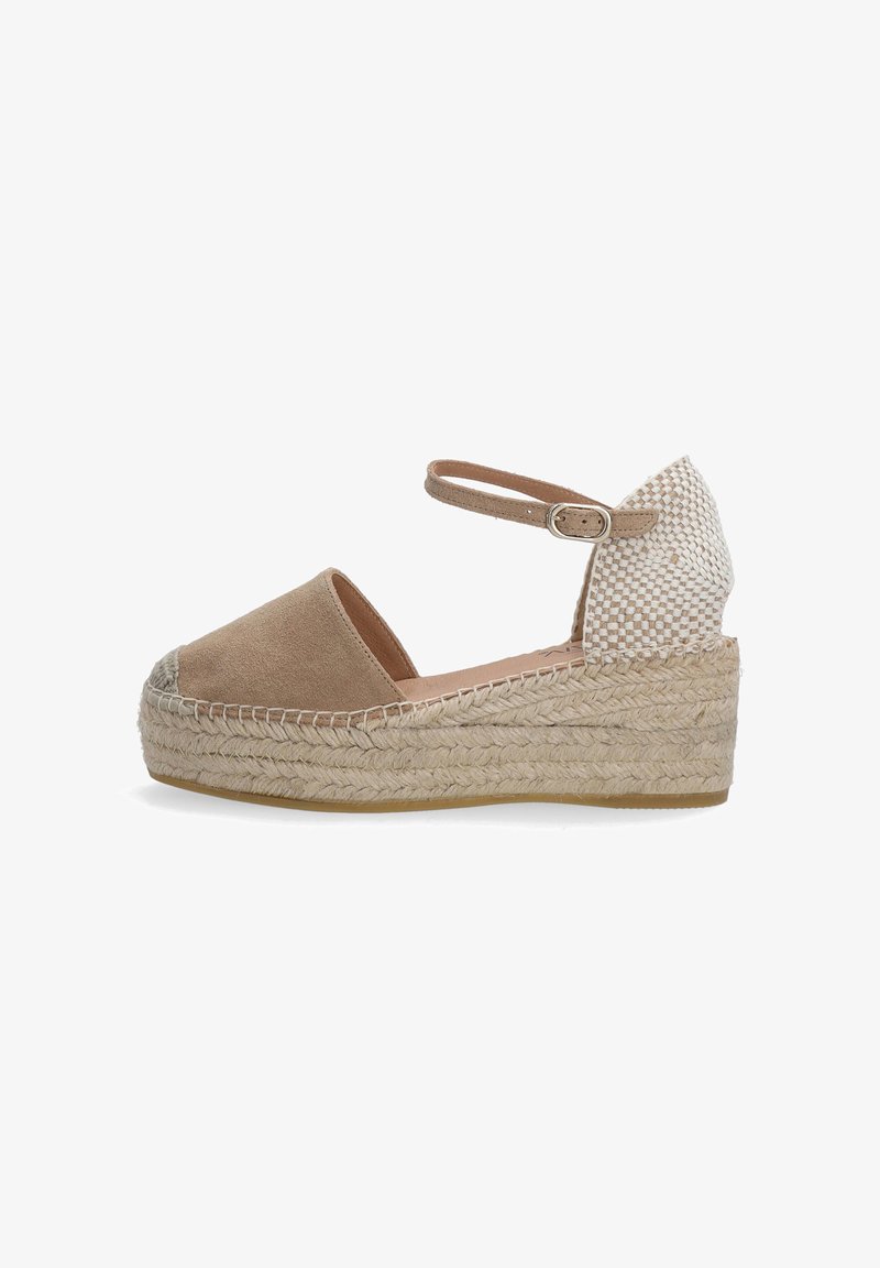 Beige suede espadrille wedge shoe with ankle strap, woven heel detail, and braided jute sole, featuring a rounded toe and casual design.